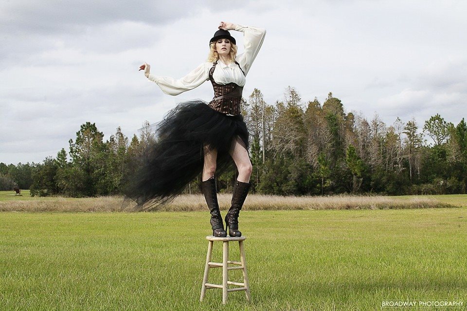 Lady in black vintage dress standing on wooden stool in the middle of a grass field
